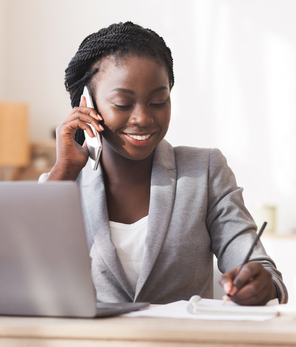 Afro Secretary Taking Notes And Talking On Cellphone In Office